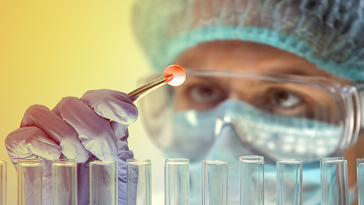 Naukowiec trzymający pensetą pigułkę nad rzędem probówek.